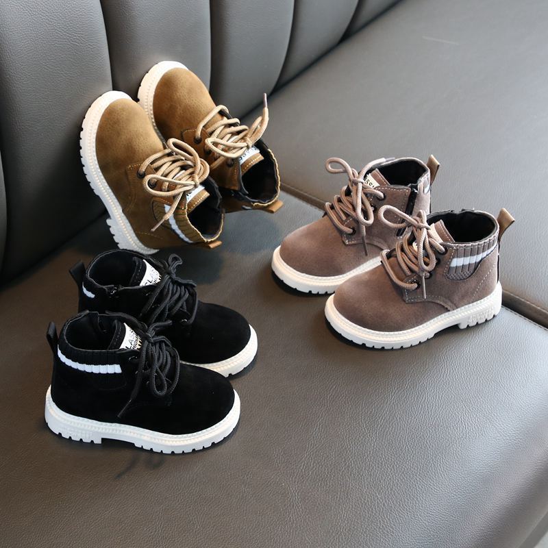 Three pairs of baby boots with soft soles in black, brown, and tan colors with laces on a gray surface