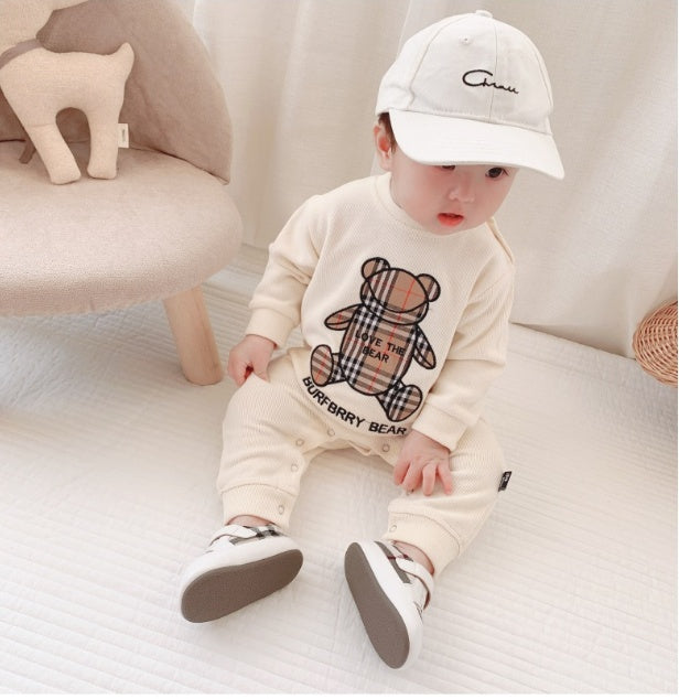 Baby boy wearing trendy baby onesies for boys in cream with bear print and white cap