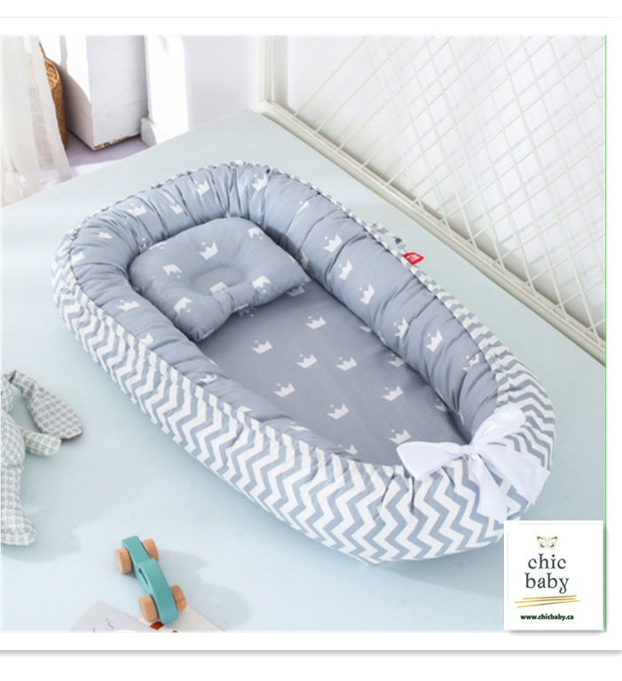 Gray and white portable baby travel crib with crown pattern and soft cushioned edges for infant comfort