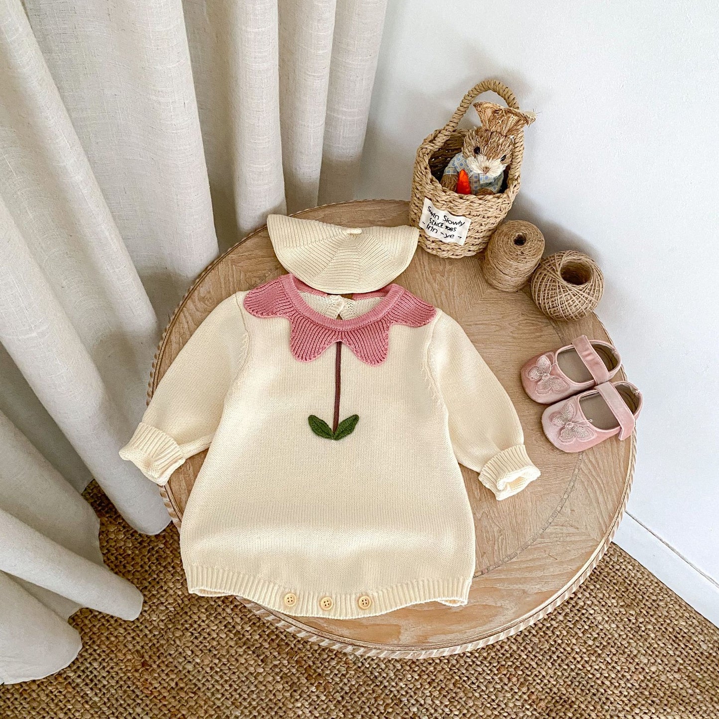 Cream floral newborn sweater with pink collar and green stem detail laid on wooden table with baby hat and shoes