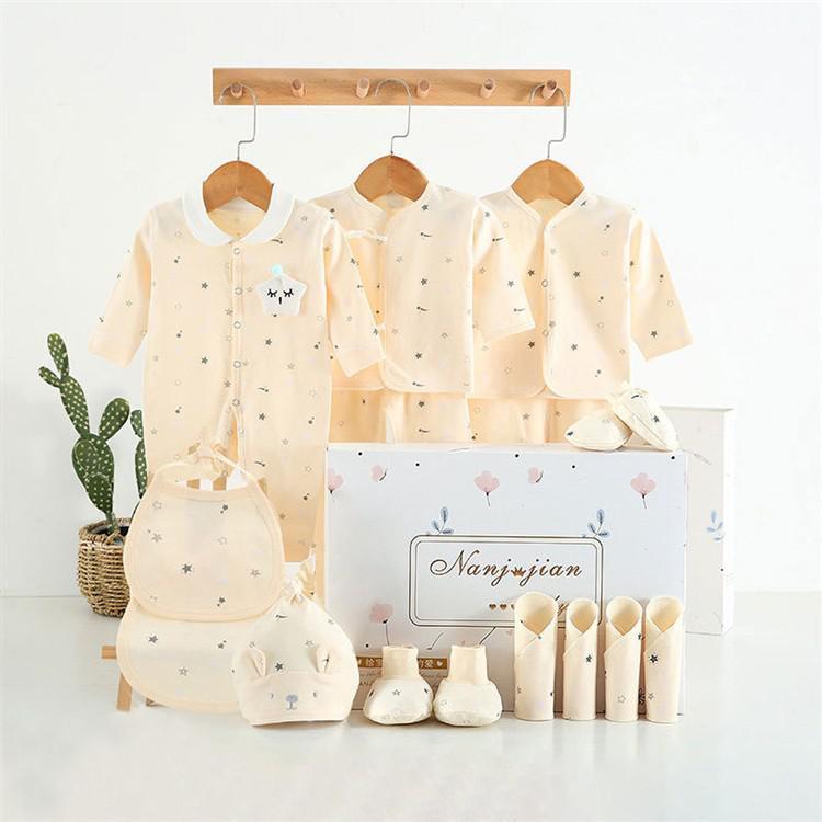 Newborn baby clothes gift set with cream-colored outfits including bodysuits hats mittens and bibs displayed with a decorative gift box