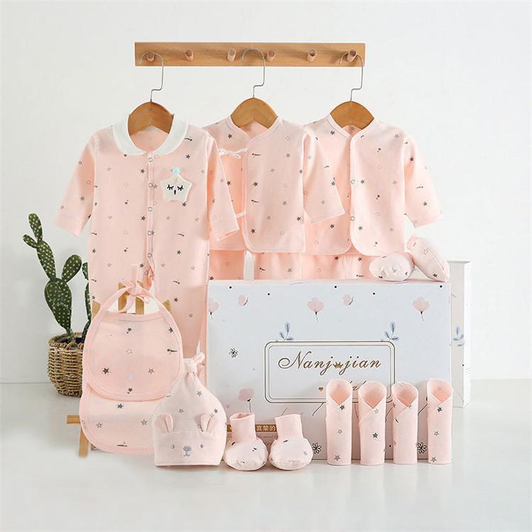 Newborn baby clothes gift set in soft pink with a onesie, hat, bib, booties, and clothing pieces displayed with gift box