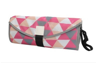 Portable baby changing pad with pink and gray triangle pattern and black strap for easy carrying