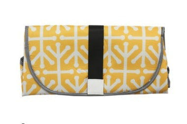Yellow and white patterned portable baby changing pad folded with black strap closure