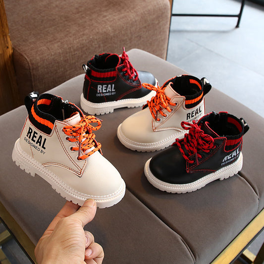 Boys and girls warm martin boots in black and white with orange and red laces displayed on a gray sofa