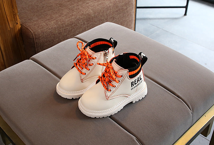 White boys and girls warm martin boots with orange laces and black cuff detail on gray cushioned surface