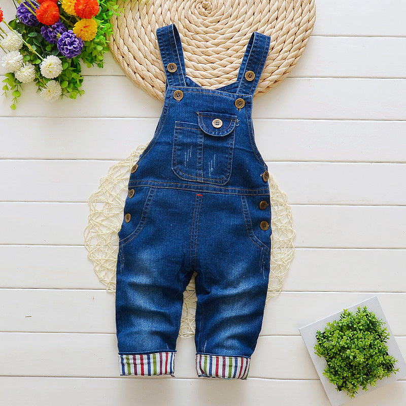 Denim bib jeans for toddlers with button straps and striped cuffs laid flat on white wooden surface