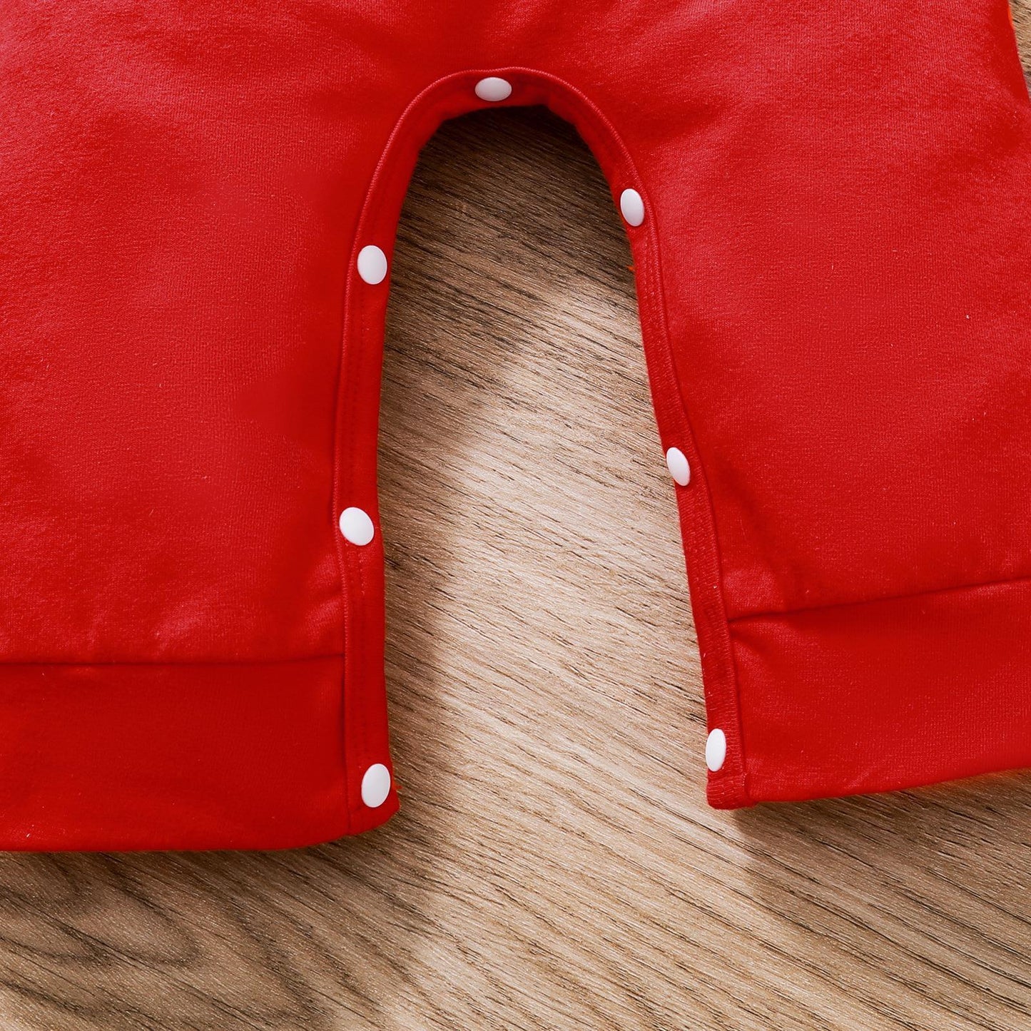 Close-up of red baby Christmas onesie with white snap buttons on wooden surface