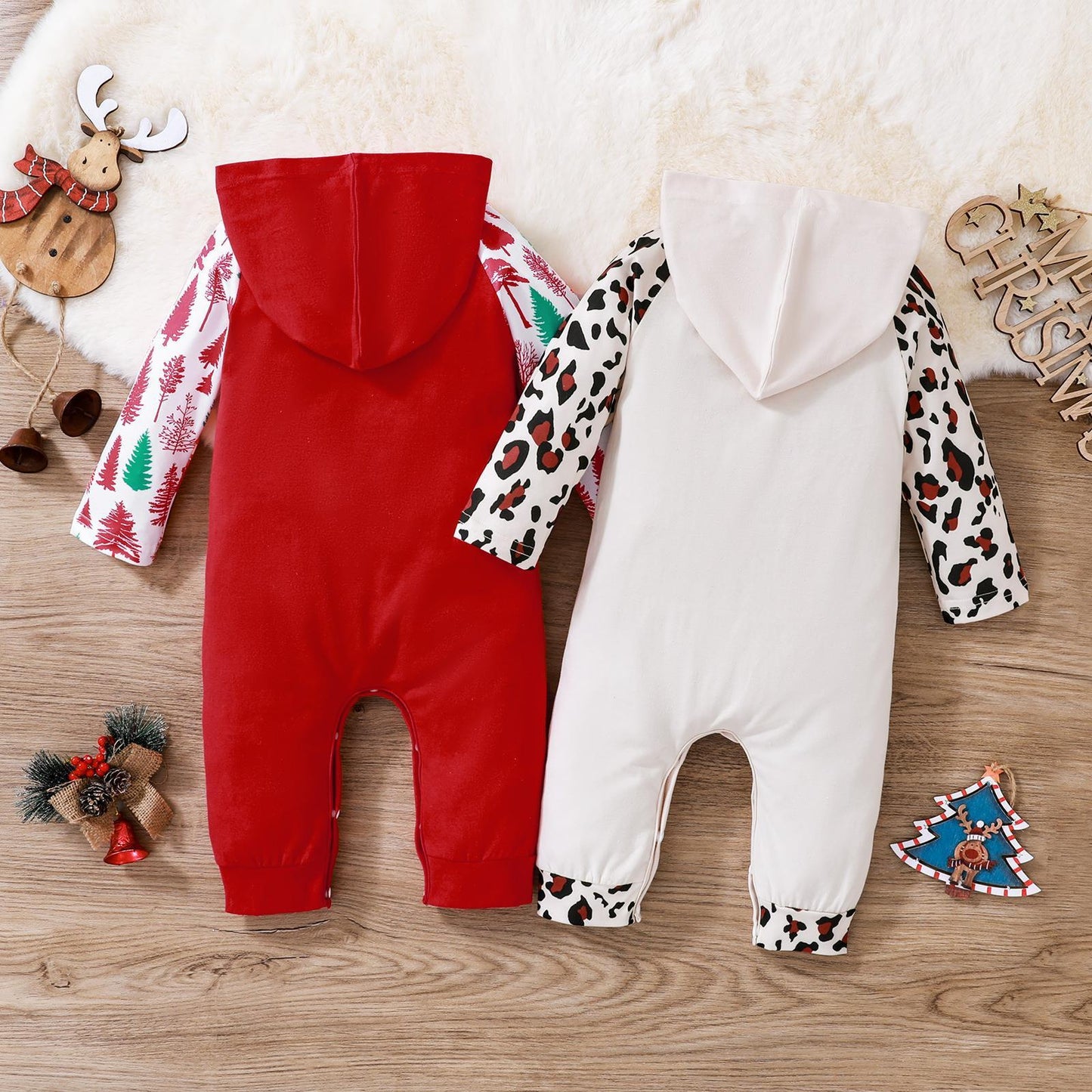 Two baby Christmas onesie outfits with red and white holiday patterns and hoods laid flat on a wooden surface