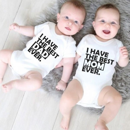 Two babies wearing matching white baby romper for summer with I have the best mom and dad ever text