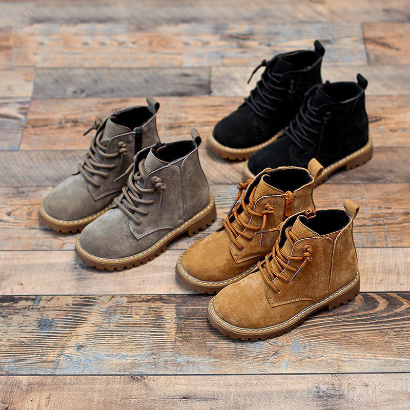 Boys black Martin boots with lace-up design and rugged soles on wooden floor alongside brown and gray boots