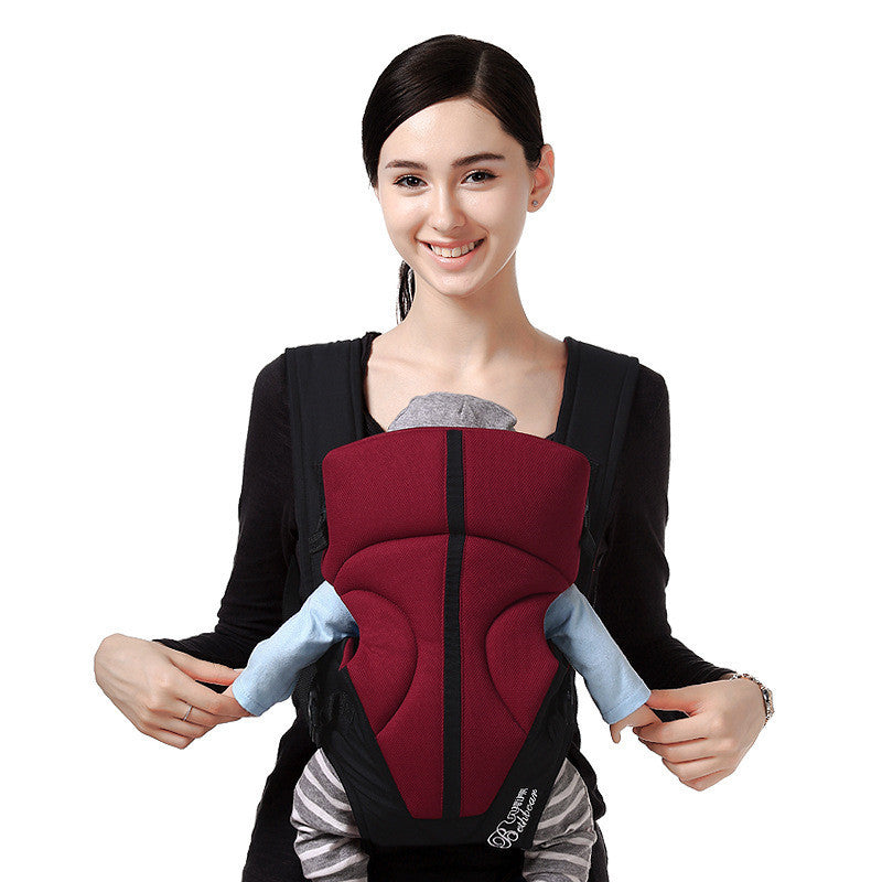 Smiling woman wearing a comfortable baby carrier in red and black with baby inside