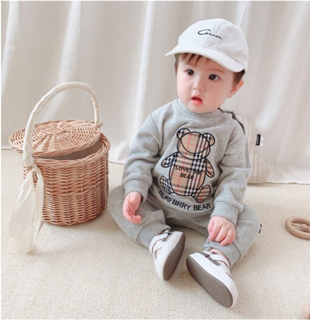 Baby boy wearing trendy baby onesies for boys with teddy bear design and white cap sitting indoors