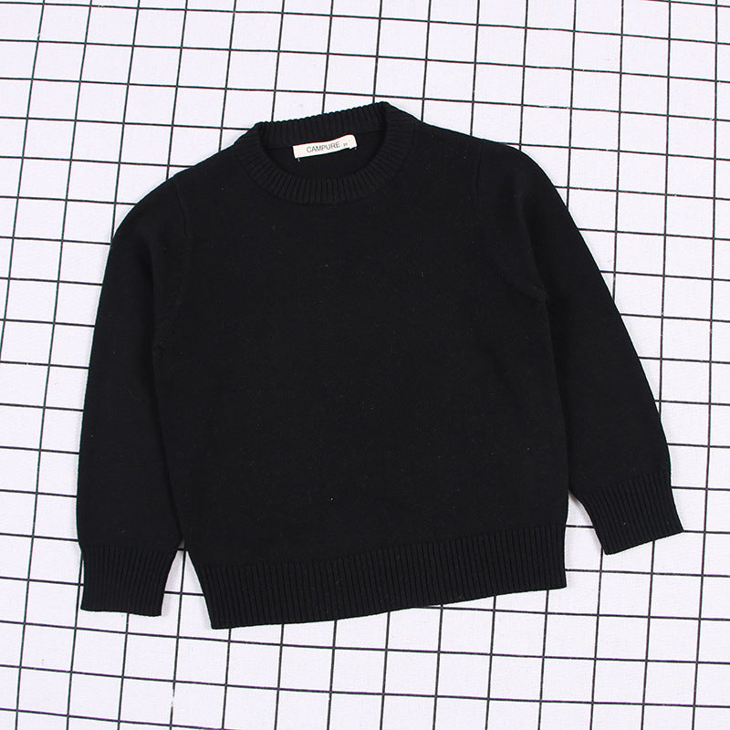Black solid color toddler sweater with long sleeves and ribbed cuffs laid flat on grid background
