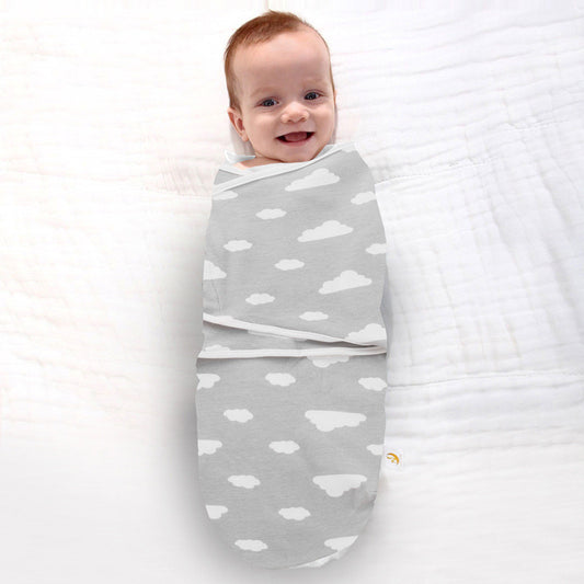 Smiling baby wrapped in a soft gray cloud print newborn swaddle on a white blanket