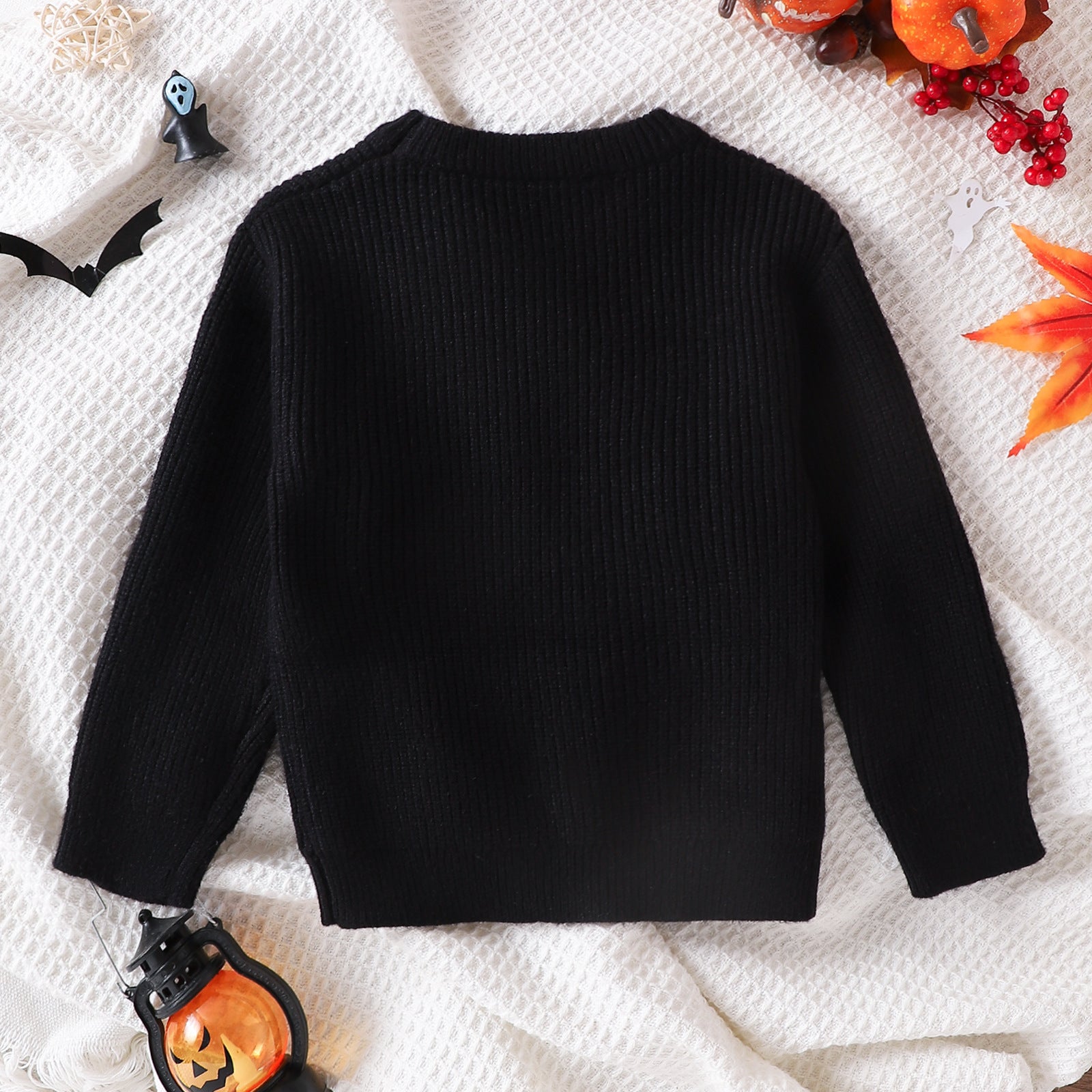 Black cute ghost sweater for toddlers displayed flat with Halloween decorations around