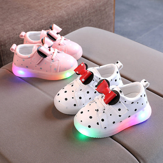 White and pink light up shoes for girls with polka dots and bow accents on gray surface