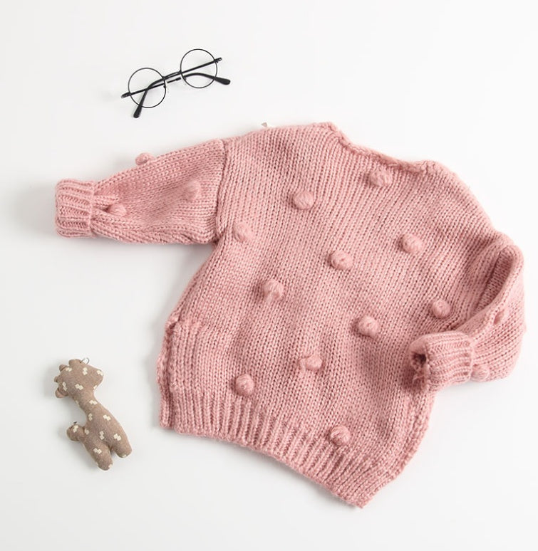 Pink knitted cute toddler cardigan for girls with textured pom pom details laid flat with toy and glasses
