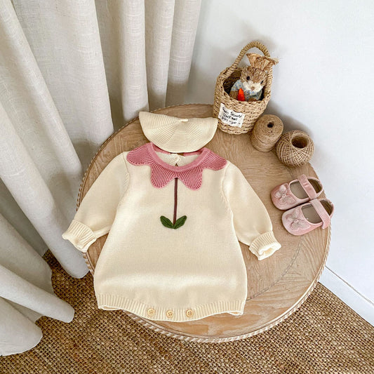 Cream floral newborn sweater with pink collar and green stem detail laid on wooden table with baby hat and shoes
