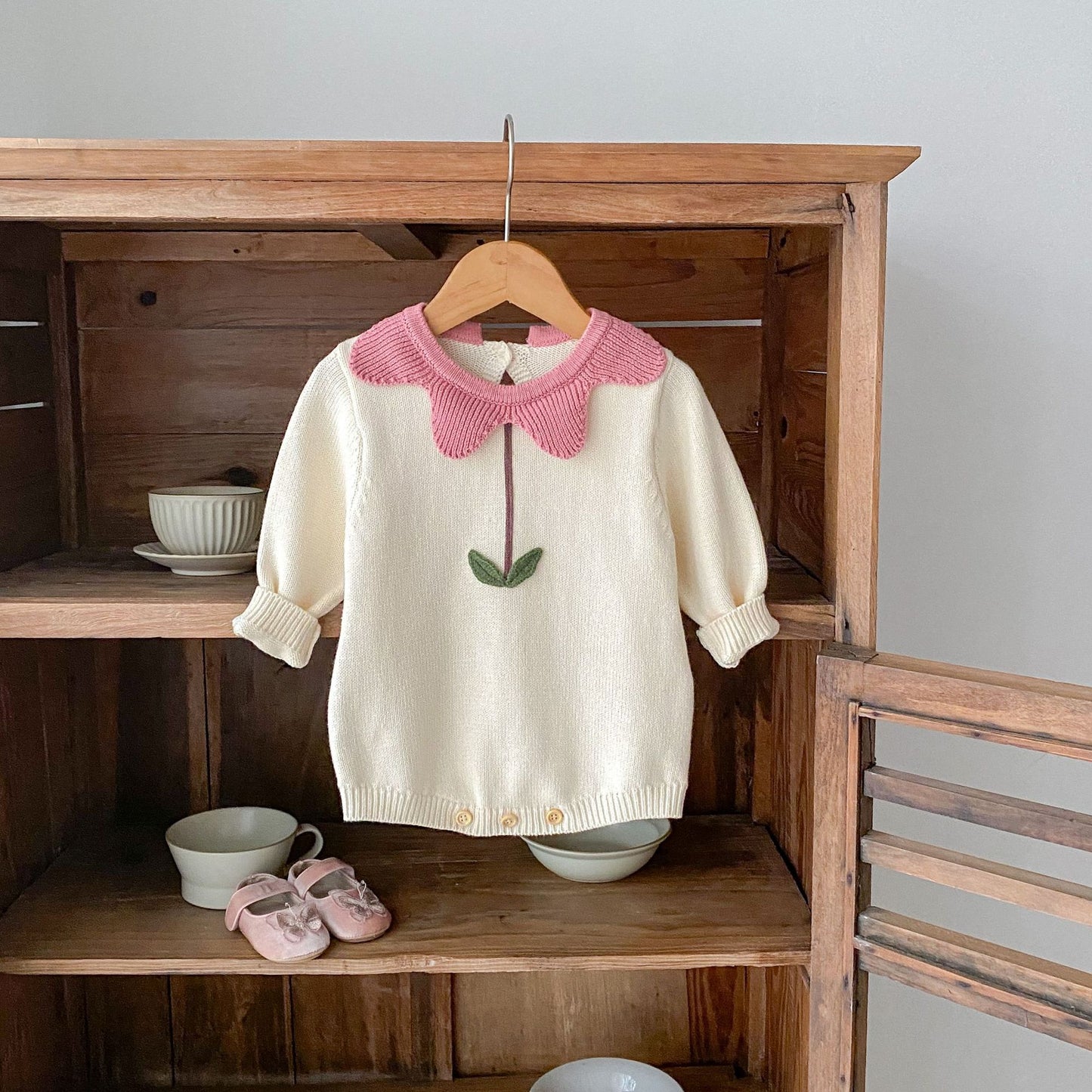 White floral newborn sweater with pink petal collar and green leaf detail hanging on wooden hanger