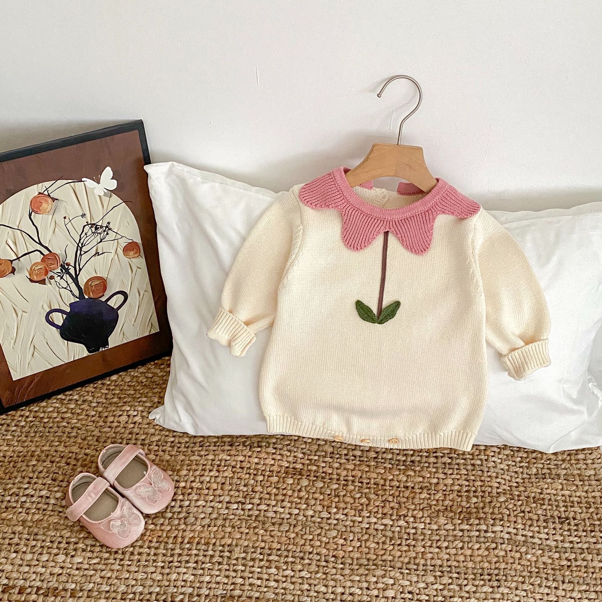 White floral newborn sweater with pink scalloped collar and leaf embroidery on a wooden hanger