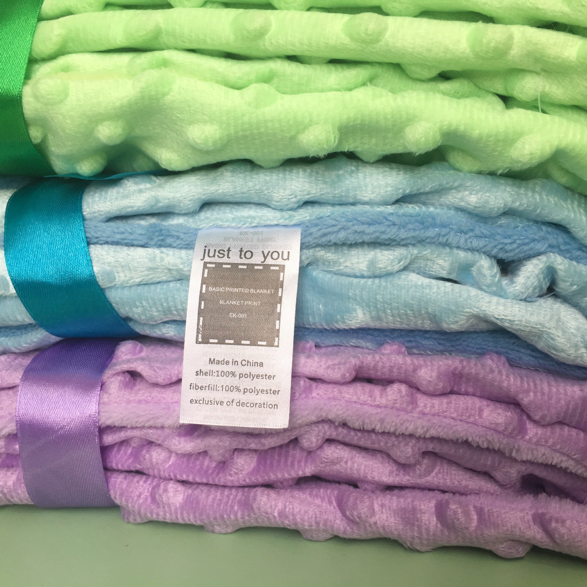 Stack of soft newborn swaddle wrap blankets in pastel green blue and purple with textured dot patterns