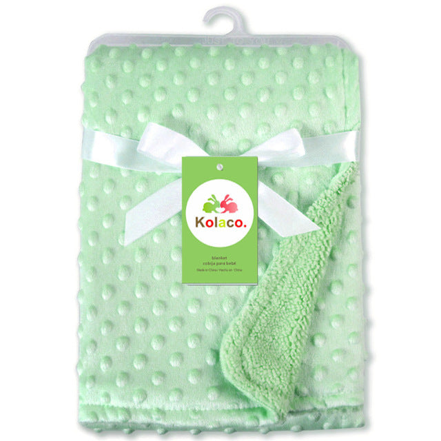 Soft newborn swaddle wrap in light green with textured dots and fleece lining tied with white ribbon