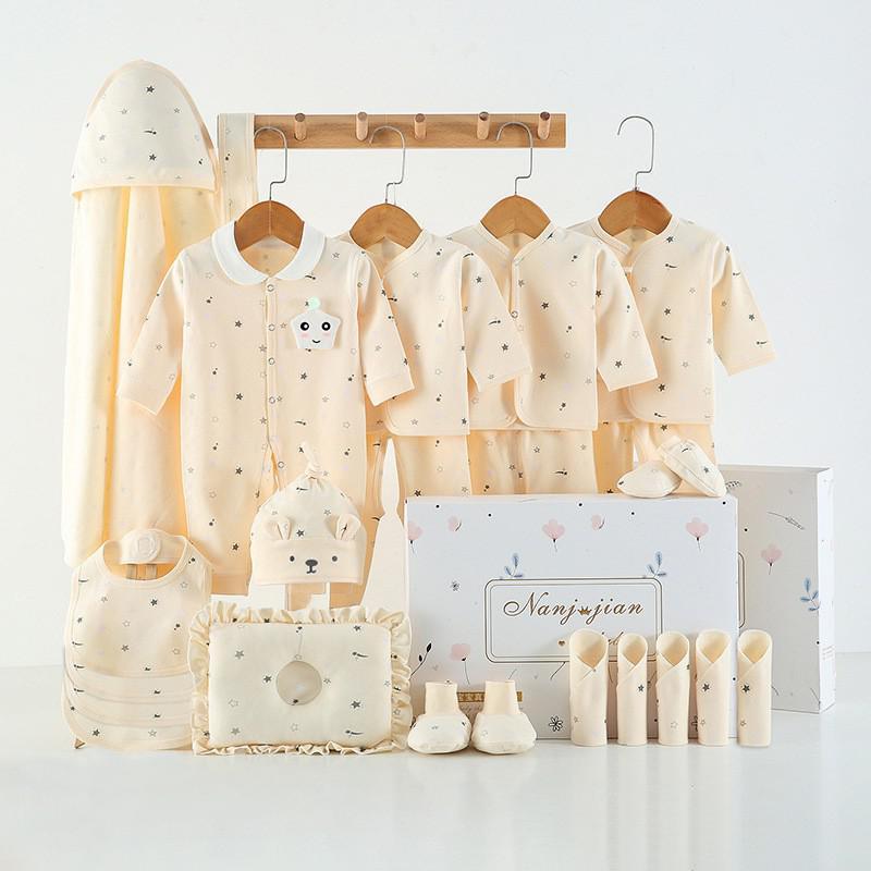 Newborn baby clothes gift set with cream-colored outfits, hats, booties, bib, pillow, and hooded towel in a decorative box