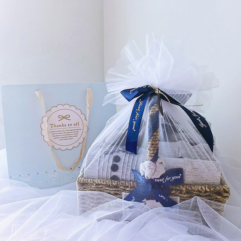 Newborn baby boy gift set packaged in a woven basket with white and blue accents and decorative ribbons