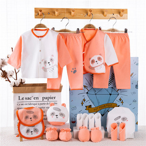 Newborn gift box with peach and white baby clothes, booties, bibs, and mittens featuring cute animal designs