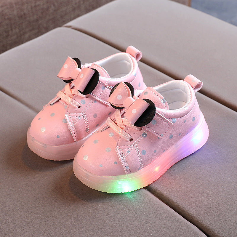 Pink light up shoes for girls with polka dots and bow accents on gray surface