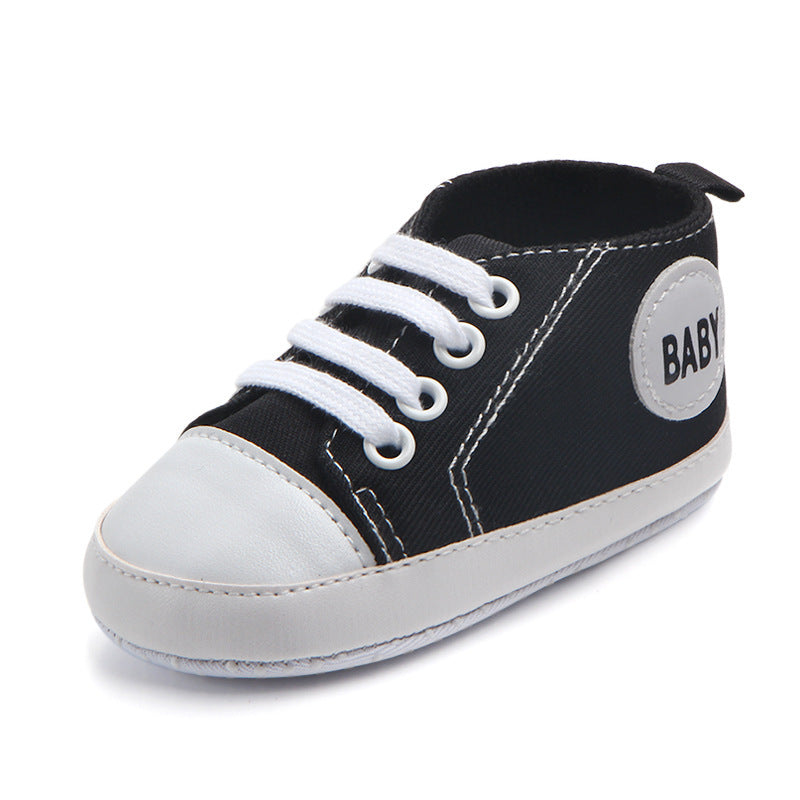 Black and white soft sole baby sneakers with laces and a baby patch on the side