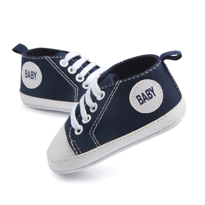 Navy blue soft sole baby sneakers with white laces and baby label on each side