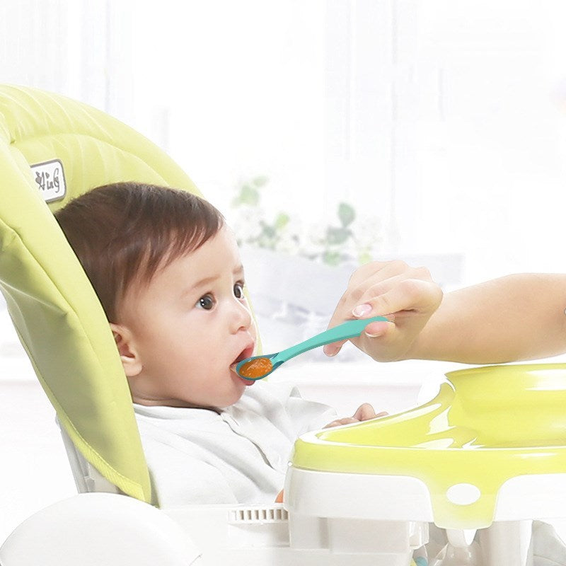 Parent feeding baby with a soft tip spoon for babies in a high chair at home