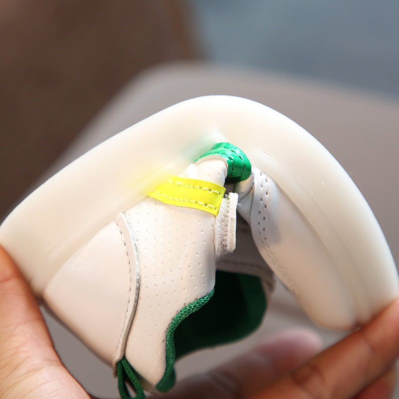 Flexible toddler velcro light up sneakers in white with green and yellow accents bending in hand