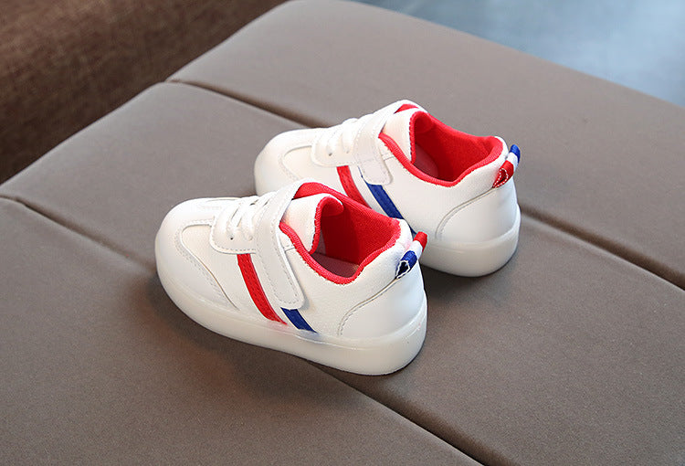 White toddler velcro light up sneakers with red and blue accents and cushioned soles on a gray surface
