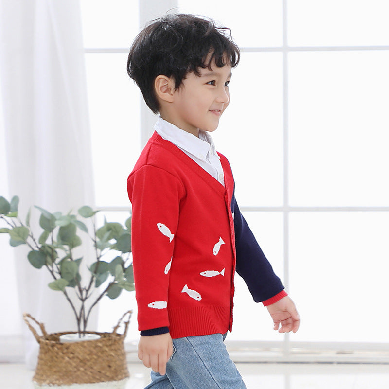 Smiling boy wearing a red and navy children's V-neck cardigan with white fish designs