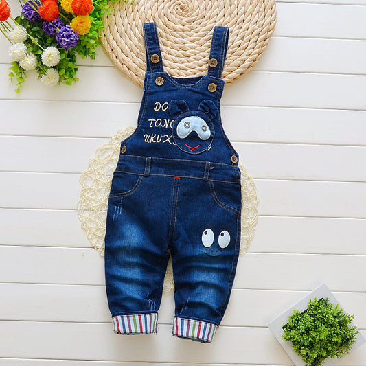 Denim bib jeans for toddlers with cute face patches and striped cuffs on a white wooden background